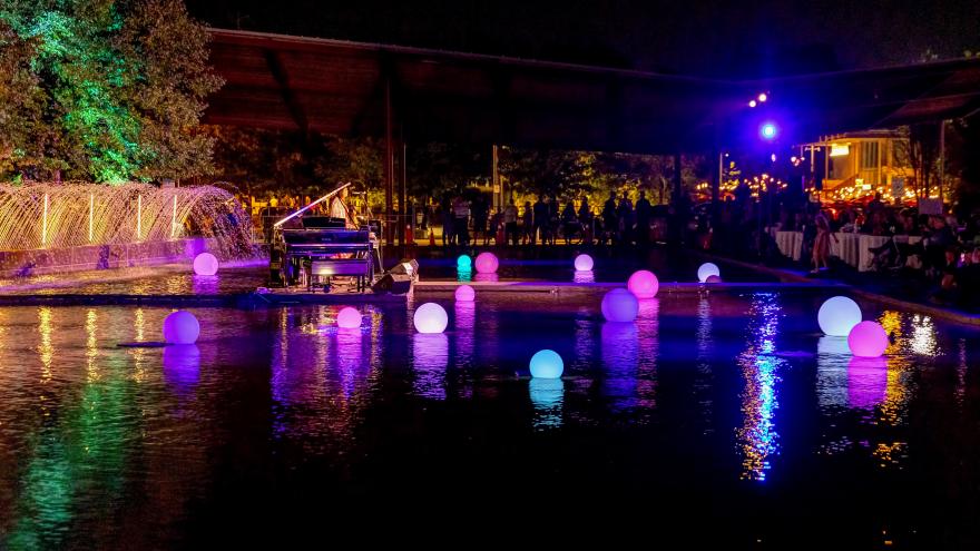 Glowing orbs float on a reflective pool at night, with a grand piano nearby.