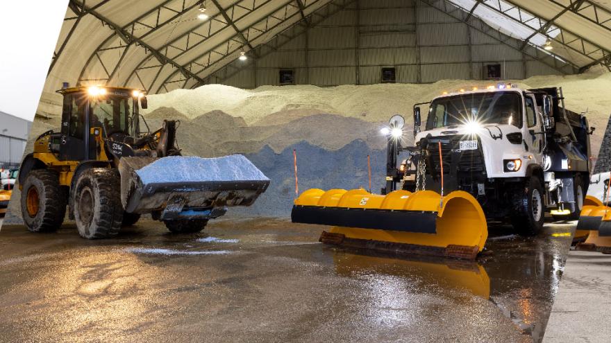 Snowplows and machinery parked in a warehouse and outdoor lot.