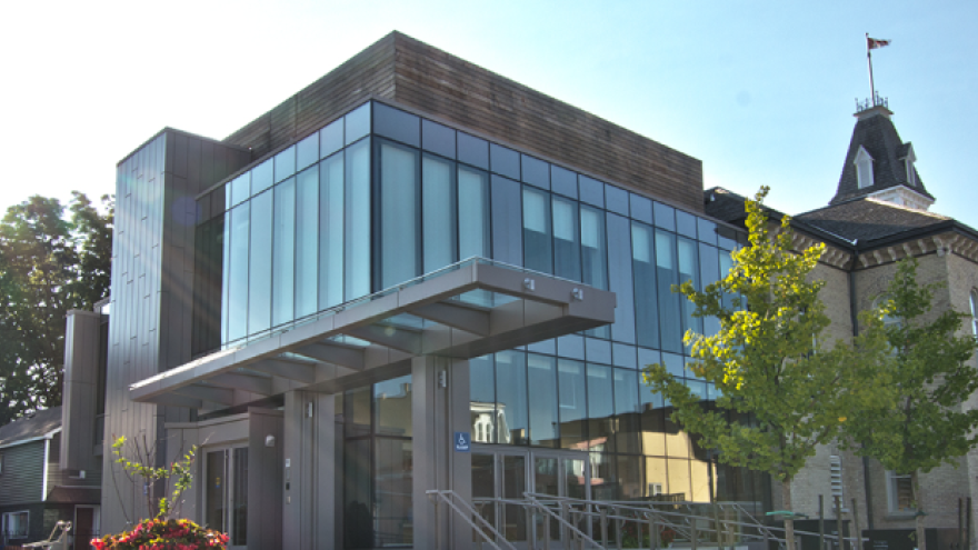 Modern glass building with a historic structure, under a clear sky.