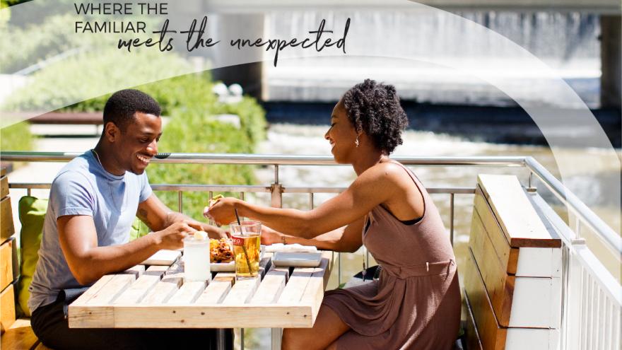 Two people happily chatting at an outdoor café by a waterfall.