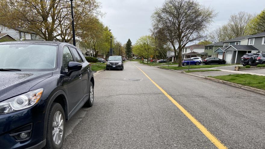 Black cars parked on a rainy wet street with houses in the background