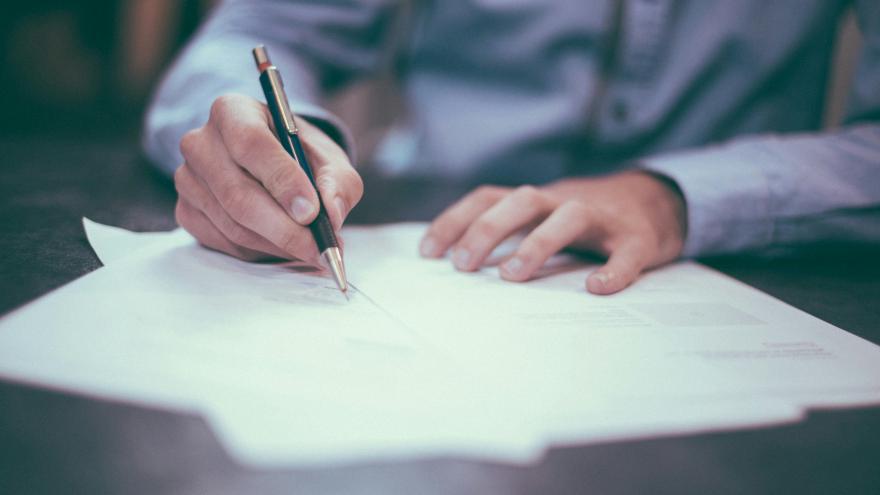 Man in dress shirt filling out a paper form on a dark wood table