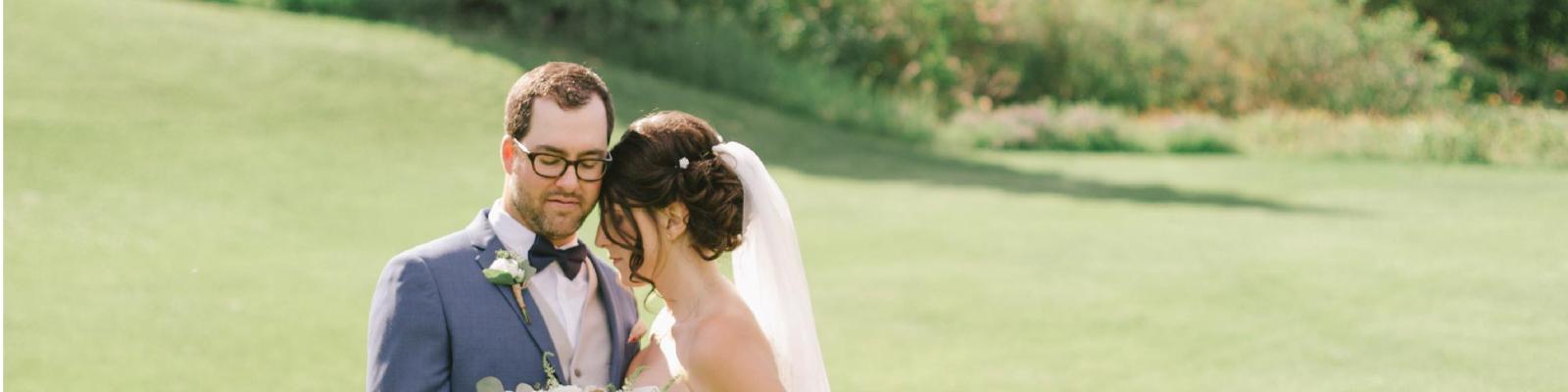 Bride and groom smiling on a sunny, grassy field.