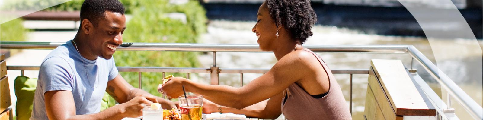 Two people happily chatting at an outdoor café by a waterfall.