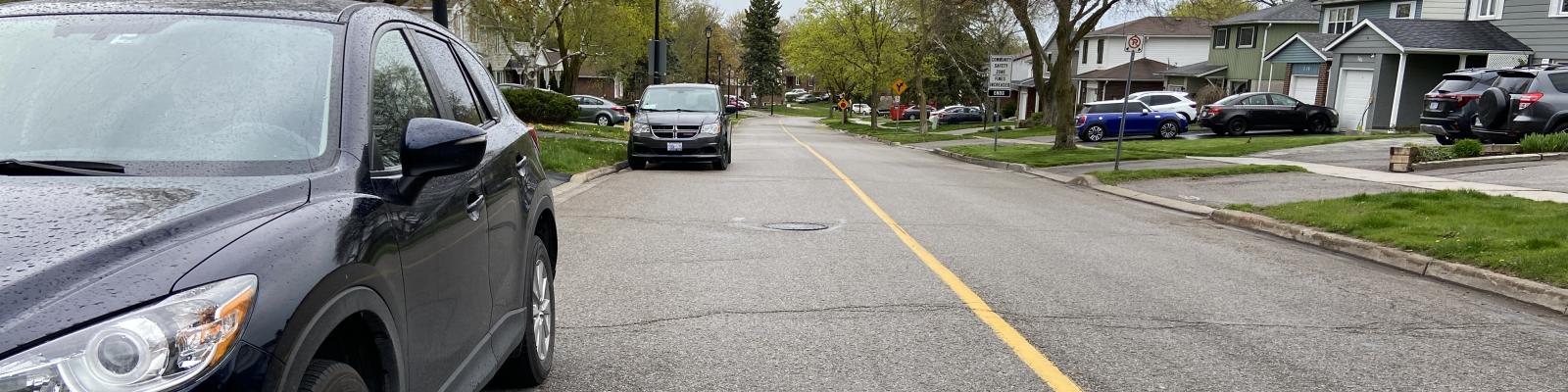 Black cars parked on a rainy wet street with houses in the background