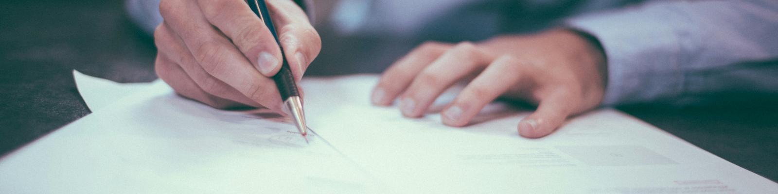 Man in dress shirt filling out a paper form on a dark wood table