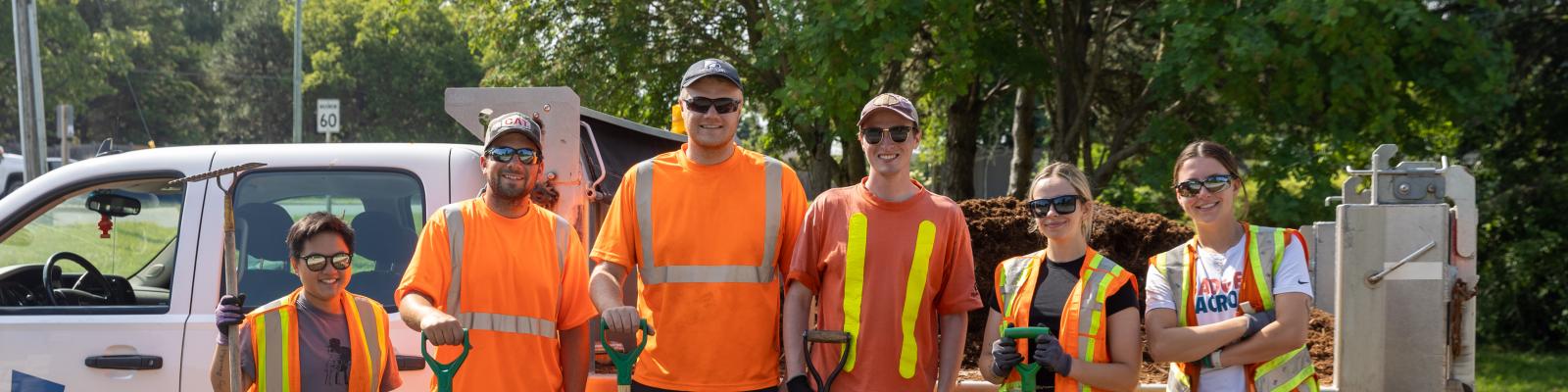 Group of people holding shovels standing in front of a truck