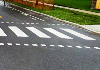 Crosswalk on wet road next to a grassy area.