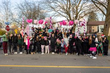 A large group of people stands in front of a decorated float with pink and white details.