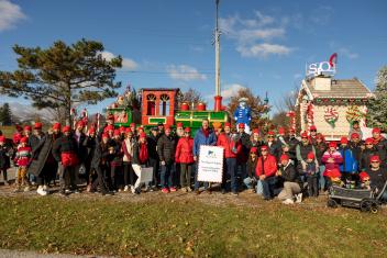Large group in red hats, posing by festive train float, clear sky.