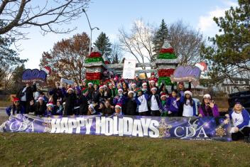 Cheerful group with Santa hats and festive banner outdoors.