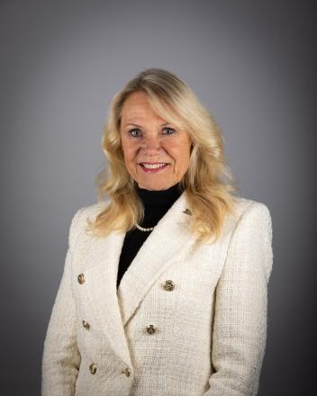 Christina Bisanz smiling in a light blazer against a gray background.