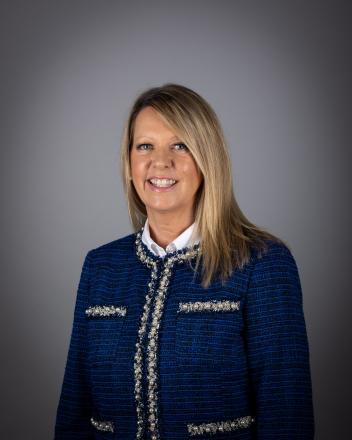 Jane Twinney smiling in a blue blazer against a gray background.