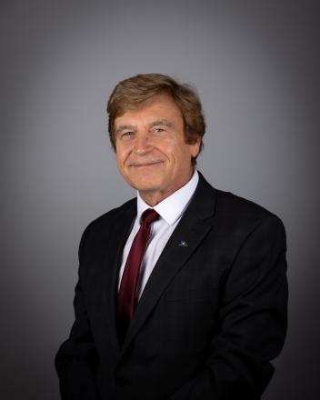Tom Vegh in a dark suit and red tie against a gray background.