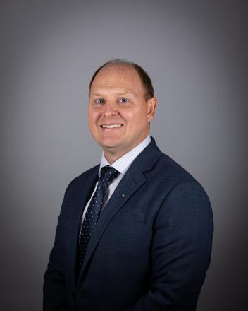 Trevor Morrison in a blue suit and tie, against a gray background.