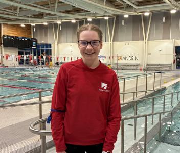 A person stands on a pool deck inside an indoor aquatic centre.