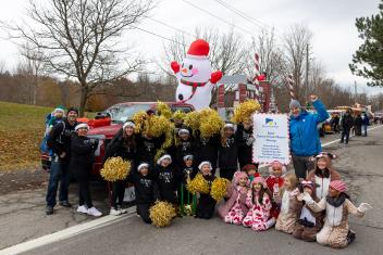 A large group of people stands in front of a decorated float with pink and white details.