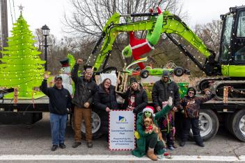 A large group of people stands in front of a decorated float with green details.