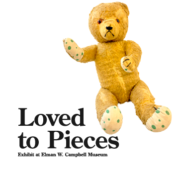 Old and tattered teddy bear next to text displaying title of the exhibit