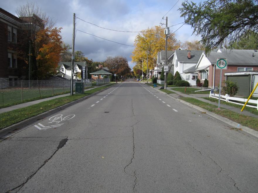 Quiet suburban street with autumn trees and cloudy sky.