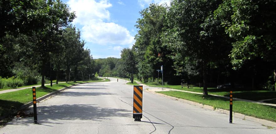 Road with trees and a traffic barrier under a blue sky.