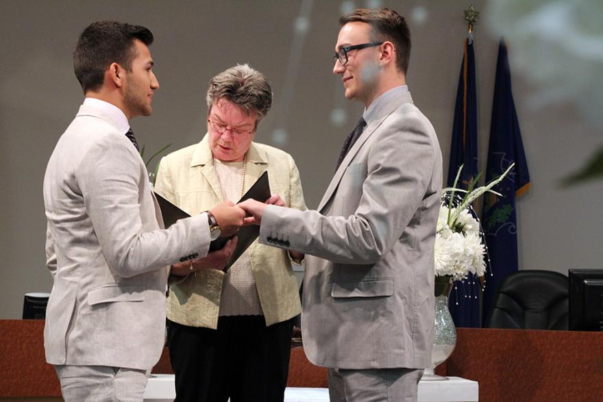 Two men in suits exchanging vows during a wedding ceremony.