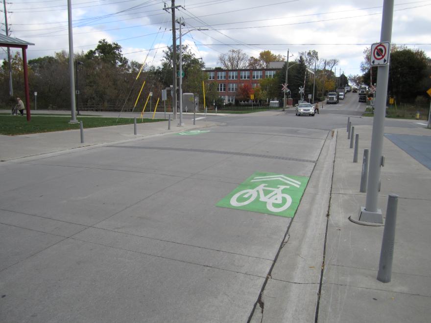 Street with marked bike lane and traffic poles, cloudy sky above.