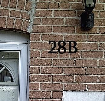 Brick wall with door and house number 28B under a black light fixture.