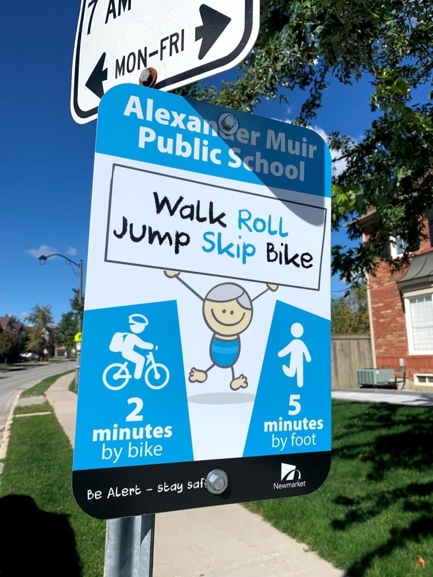 School sign showing walking and biking times, decorated with cartoon character.