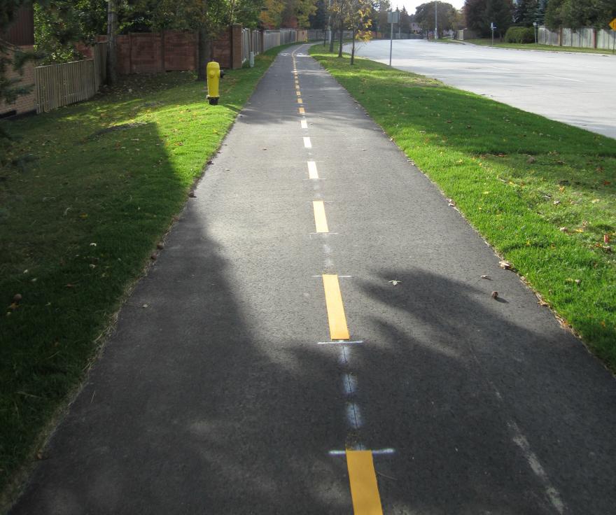 Paved pathway with yellow centre line, flanked by grass.