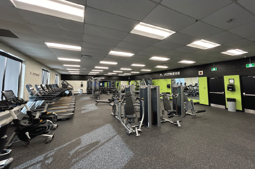 Spacious gym with exercise machines and bright lighting.