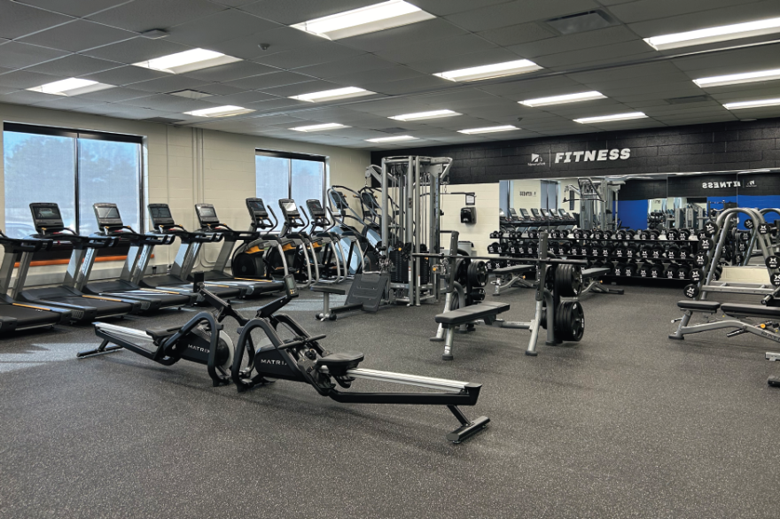 Spacious gym with treadmills, weight machines, and free weights, well-lit with large windows.