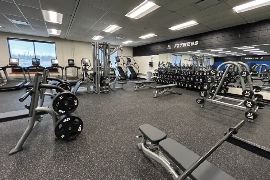 Spacious gym with weights, machines, and treadmills in bright lighting.
