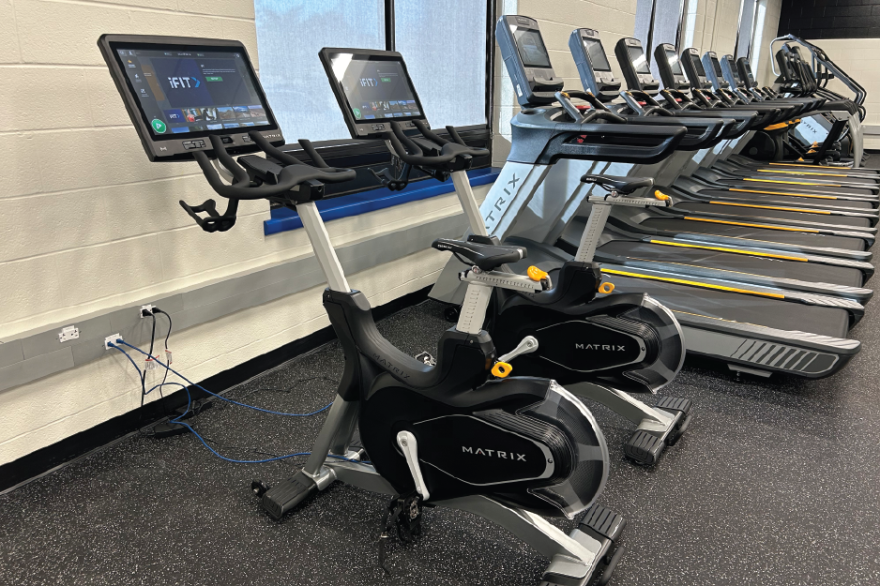 Stationary bikes and treadmills in a gym, lined up against a wall.