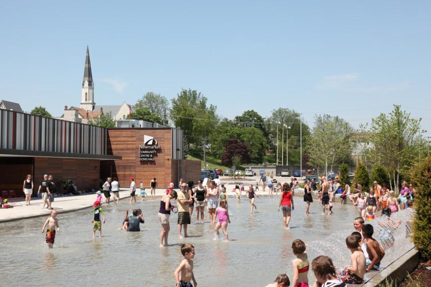 People enjoying a shallow outdoor pool on a sunny day with a church in the background.