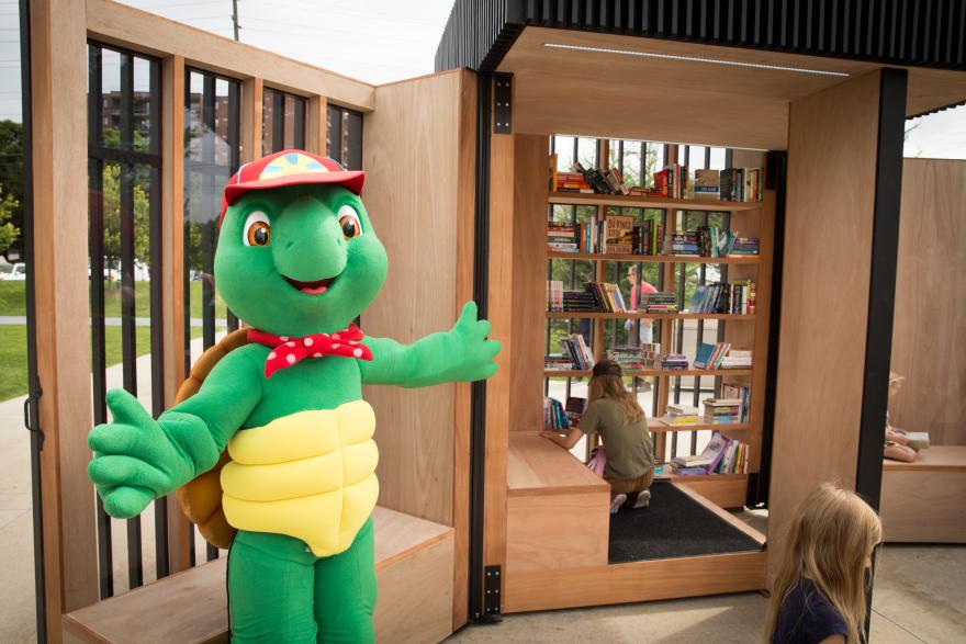 Franklin the turtle stands near the Story Pod as children read.