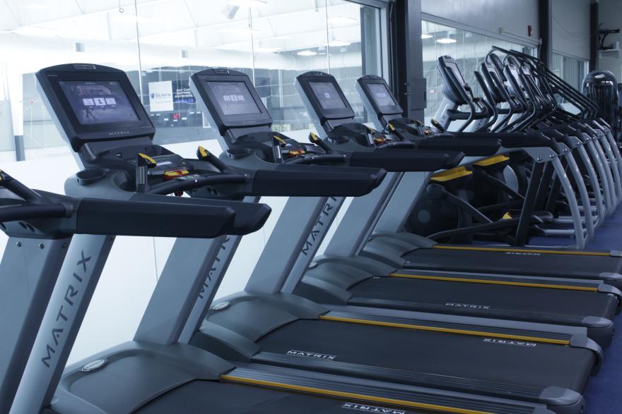 Row of treadmills in a brightly lit gym.