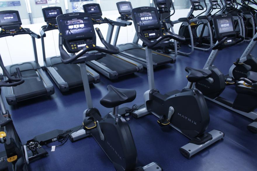 Treadmills and exercise bikes in a gym with blue flooring.