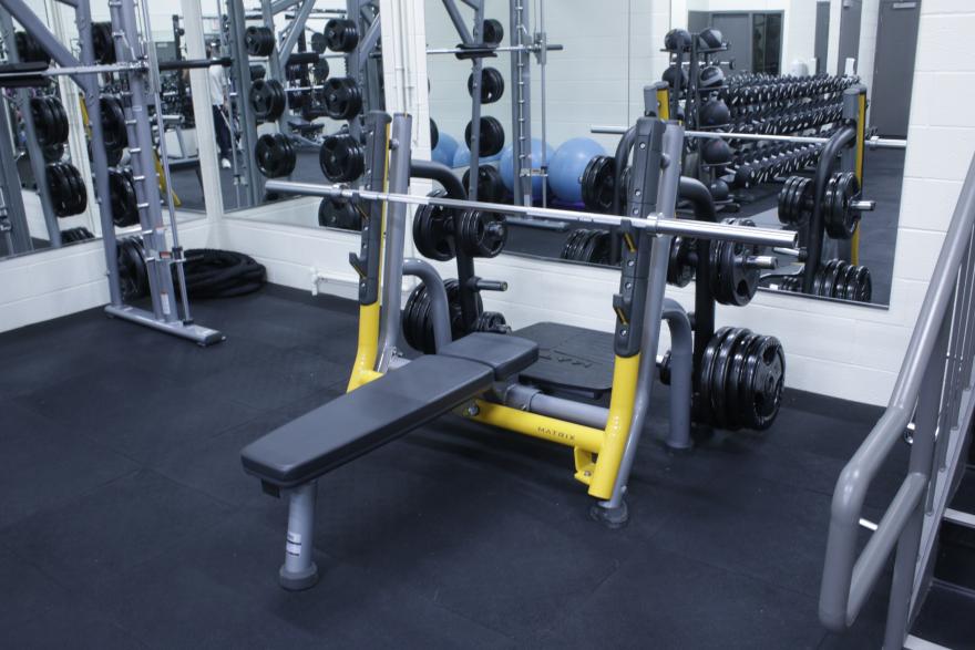 Bench press with weights in a gym, surrounded by mirrors and dumbbells.