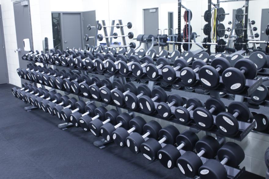 Rows of dumbbells in a gym with mirrored walls.