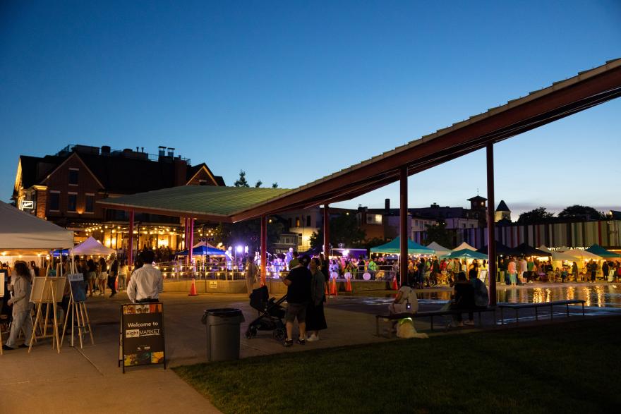 Outdoor market at dusk with tents and lights.