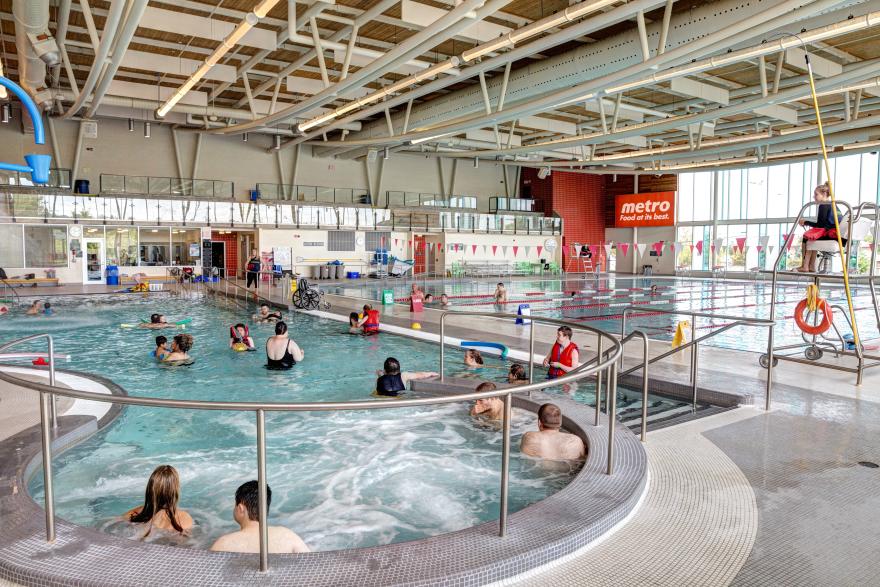 Indoor pool with people swimming and sitting in a large, bright room.