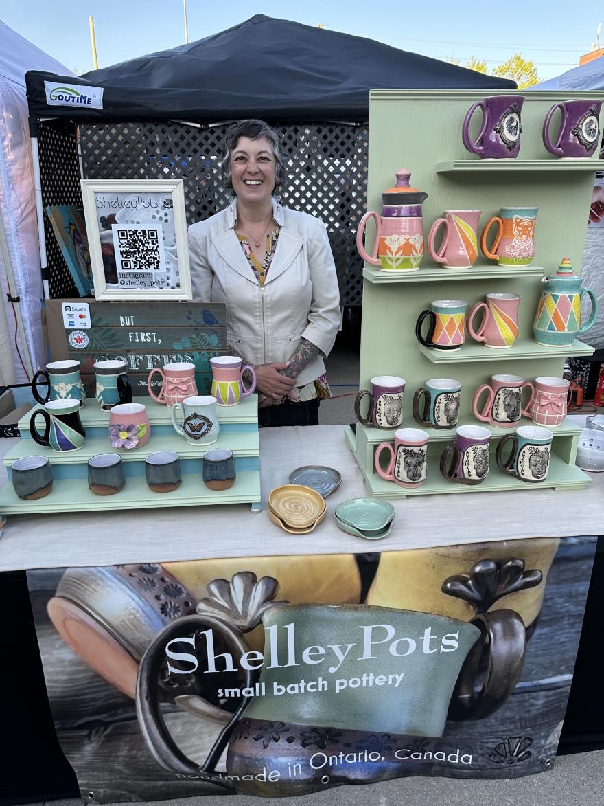 Potter in booth with colorful mugs on display shelves.