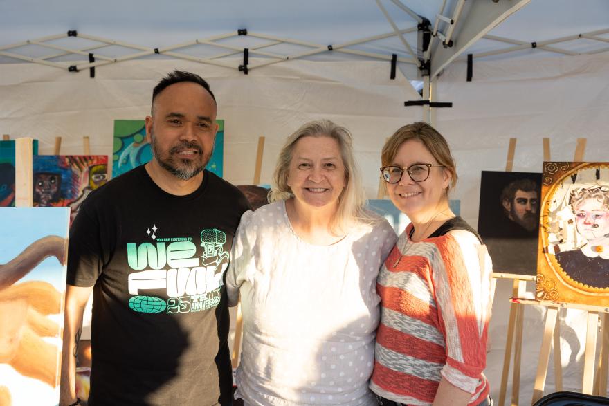 A group of three people smiling under a tent at an art fair.