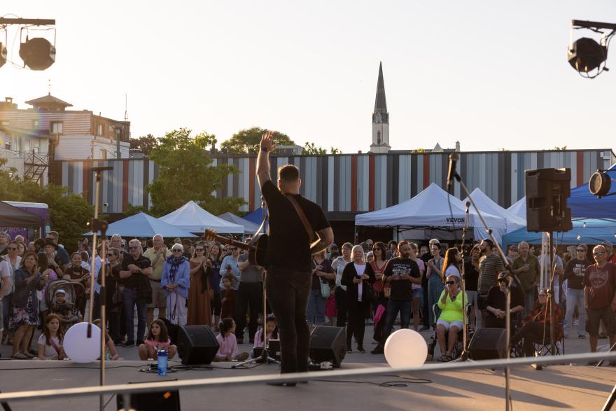 Performer on stage facing a large outdoor crowd at sunset.