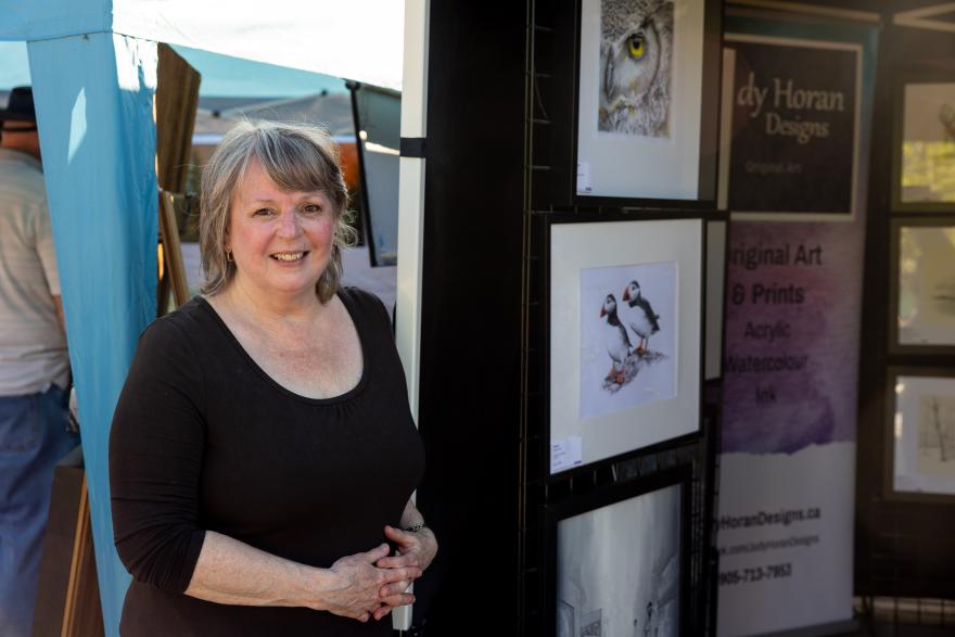 Smiling woman stands near art display with framed animal prints.
