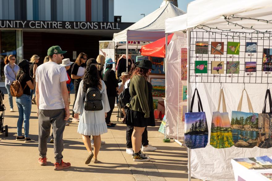 Outdoor market with people browsing art and handmade items.