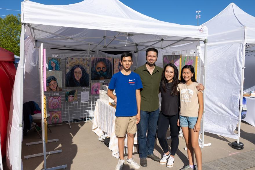 Family posing at an art booth under a white tent on a sunny day.