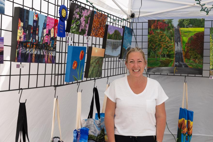 Art vendor in a tent smiling, surrounded by colorful paintings.