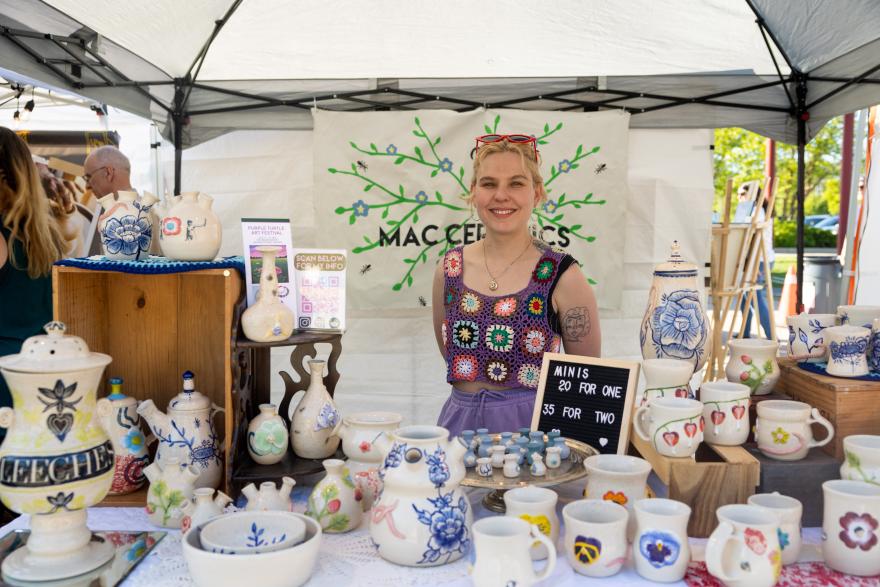 Vendor with colorful ceramics displayed on a market stall under a canopy.